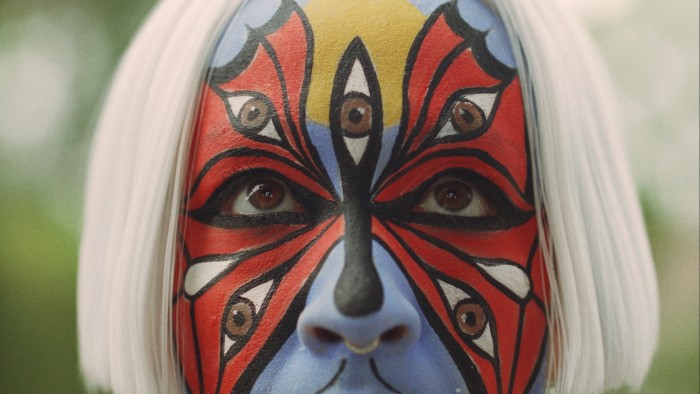 Close-up of a face painted with a large red butterly whose wings have brown eyes