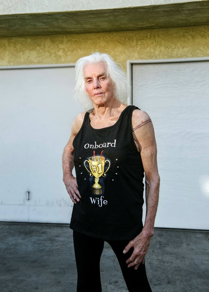  A woman stands in front of a garage wearing a vest that says ‘onboard wife’ and has a trophy on it