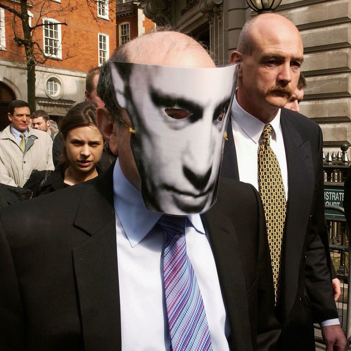 Boris Berezovsky walks out on to the street wearing suit and tie — and a Vladimir Putin face mask