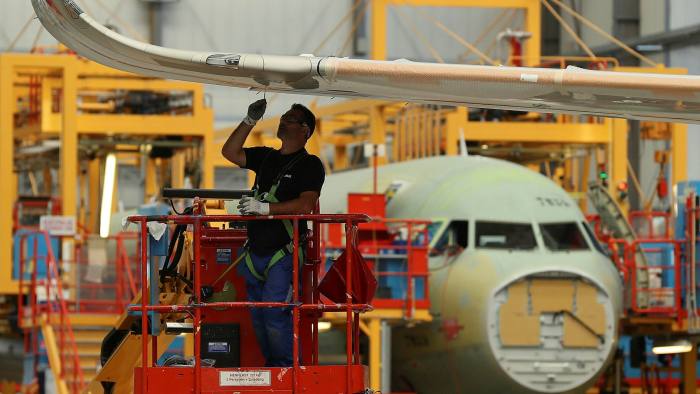 A man works on a wing of a passenger plane in an assembly hall