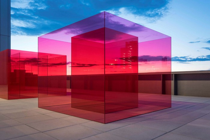 A large pale red glass cube contains a much redder glass cube, sitting on a terrace