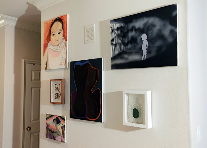 An arrangement of small paintings by different artists on a white wall