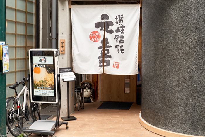Genki entrance, with an advertising board on the left, and a fabric printed with Japanese words hang from the top of the door