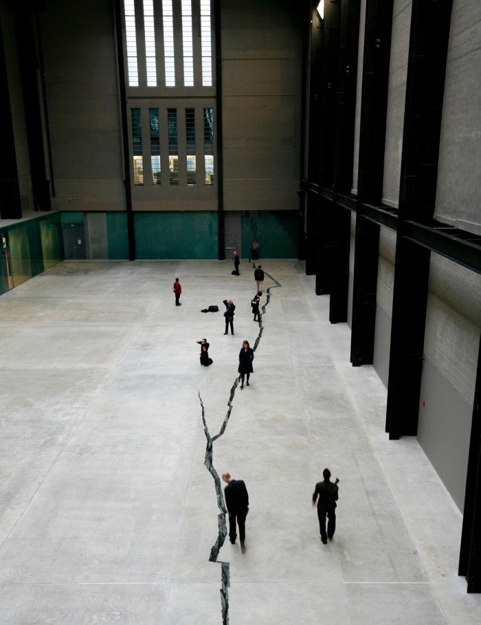 View from above of people looking at a long snaking crack in a grey concrete floor