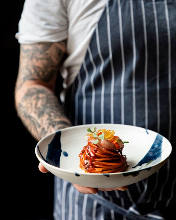 Barabba owner Riccardo Marcon’s tattooed arm and hand holding a bowl of spaghetti with gambero rosso and preserved candied lemons