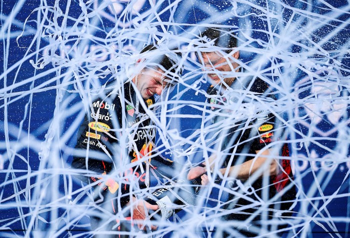 Two men from the F1 Oracle Red Bull Racing team celebrate their win on the podium. White ribbons are all over the place