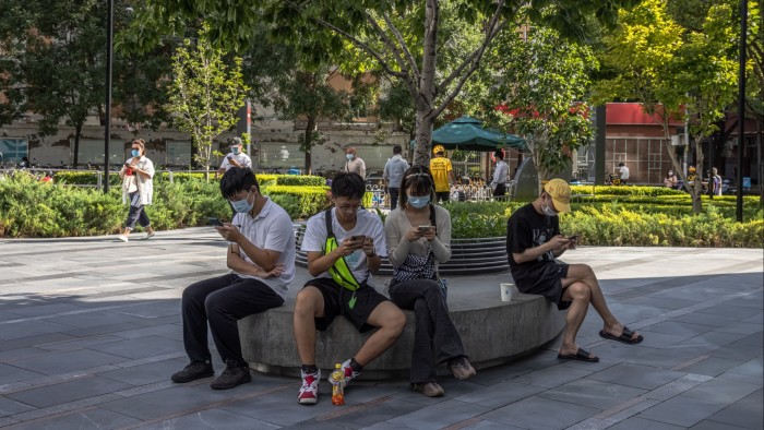 Young Chinese people use their phones as they sit in the shopping and residential area of Sanlitun in Beijing