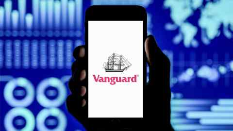 A man holds up an iPhone which displays the Vanguard Group logo