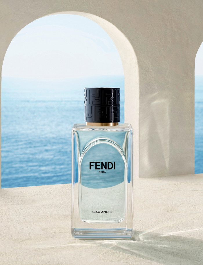 A rectangular bottle with black lid on top of a cream surface. In the background is a white arch and beyond is blue sea