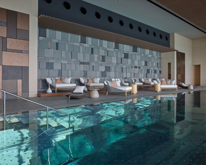 The pool in the hotel’s spa, with daybeds at a remove from its edge, against a brown and grey tiled wall