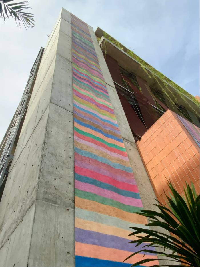 An exterior shot of a tall concrete building with a striped art work in the form of a banner extending down the length of it