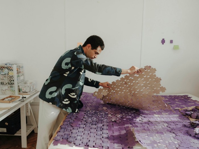 A man lifting a sheet of purple matchbox inners woves together