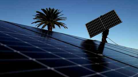A worker installs solar panels onto the rooftop of a residential property