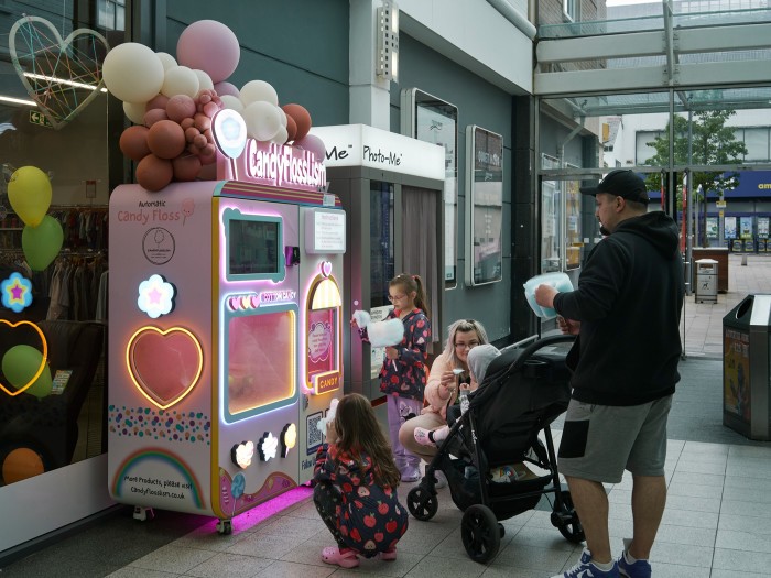 A man and women with three little children stand at an automatic candy floss machine in a shopping centre