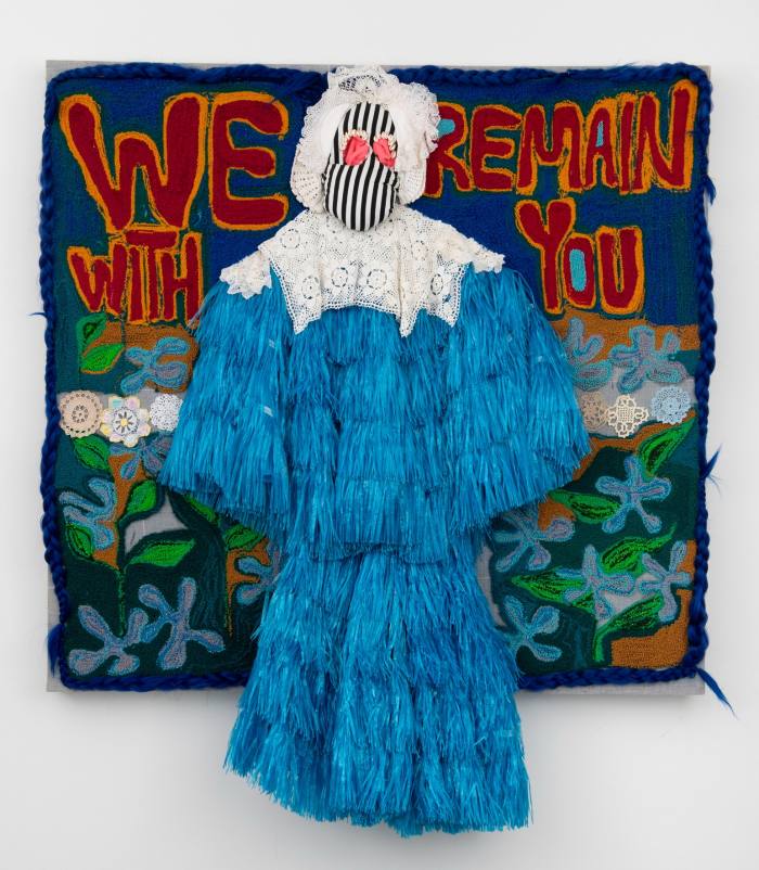 Straw doll on a felt background with words ‘We remain with you’ in letters