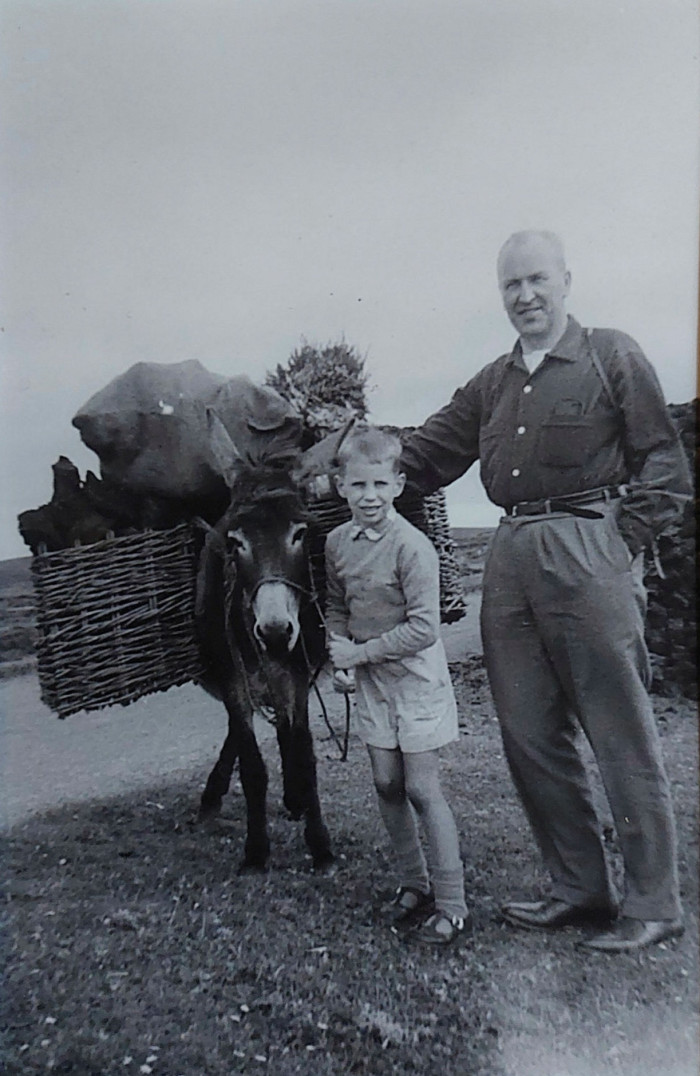 A photograph of Stanley Stewart as a boy with his father, leading a donkey loaded with peat