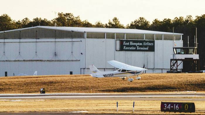 A light aircraft lands outside East Hampton Airport, in front of a large hangar
