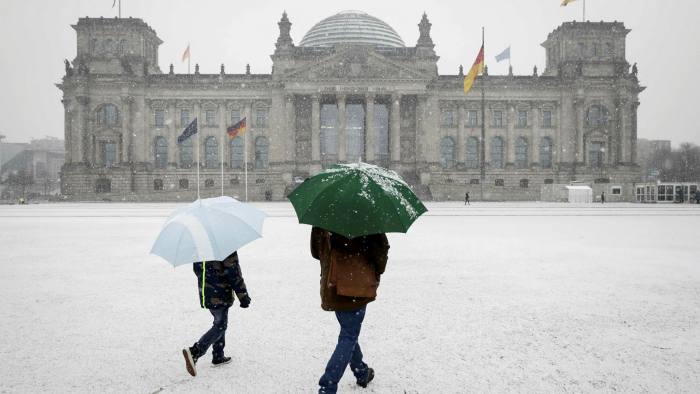 People with umbrellas walk towards a snowy Bundestag