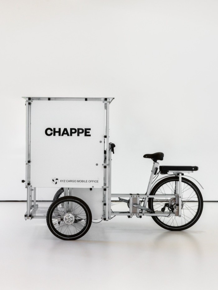 A cargo bike has a white box-cubicle on the back