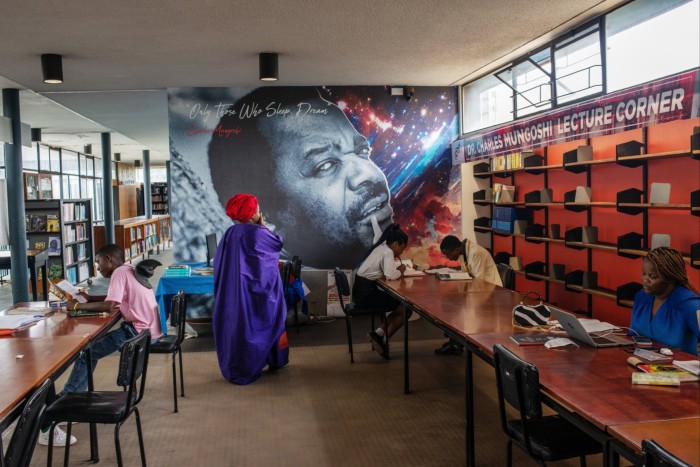 Writer Petina Gappah stands in a library named after her with teenagers are reading books at the desks 