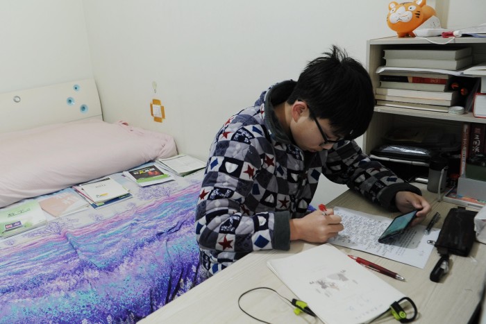 A high school student has an online class via his smartphone at home on March 9 2020 in Meishan, Sichuan Province of China. 