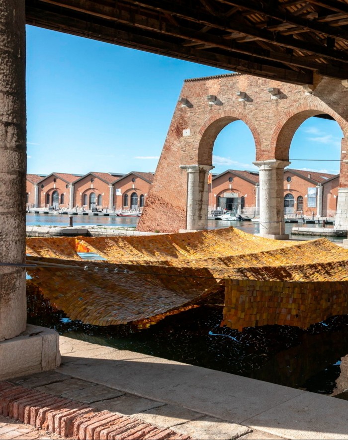A large fabric artwork draped beneath large brick columns outside