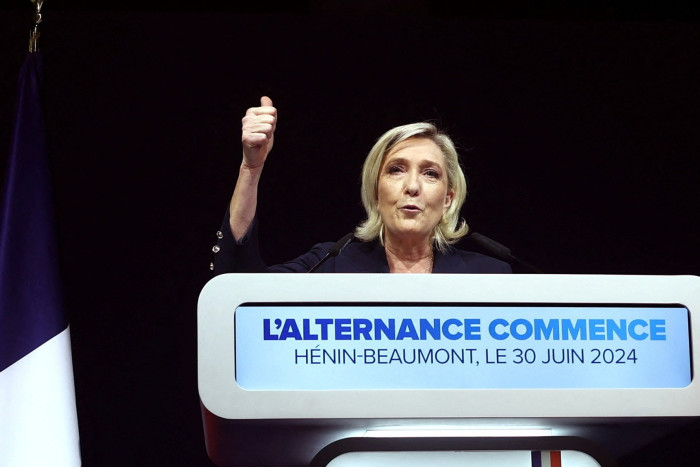 Marine Le Pen raises her right hand as she gives a speech 