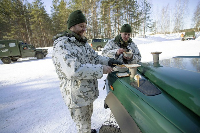 Two Finnish soldiers eat rations beside their vehicle