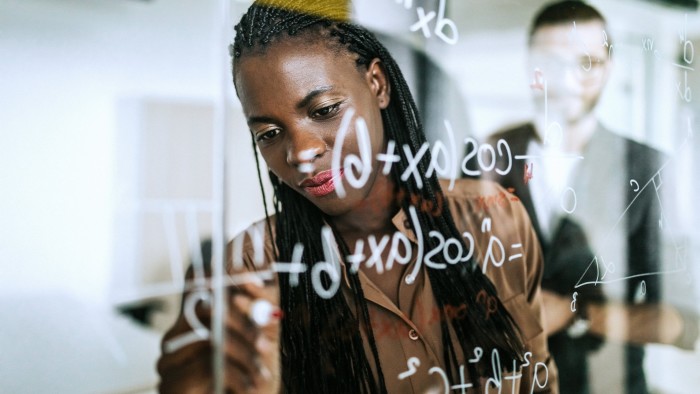 A woman writes mathematical formulas on a transparent wipe board 