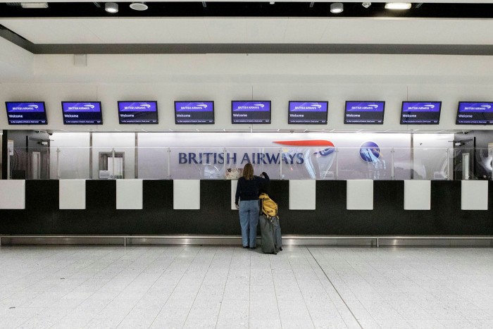 A woman inquires at a near-empty British Airways counter at London Heathrow Terminal 3