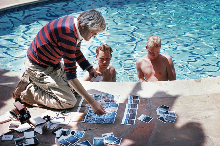 man looking at photos beside a pool; two other men in the pool