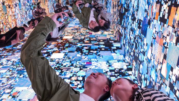 A couple take a selfie with ‘Machine Hallucinations Space: Metaverse’, by artist Refik Anadol