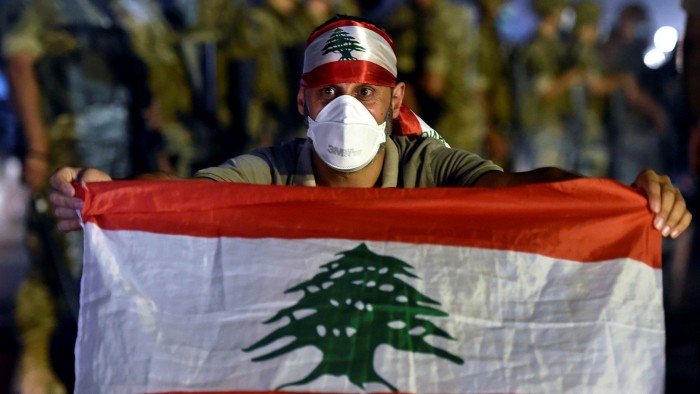 An anti-government protester poses with a national flag in front of Lebanese army soldiers during a protest in Jal El Dib, north of Beirut, on Sunday
