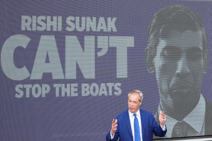 Nigel Farage delivers a speech in front of a campaign advert featuring an image of Britain’s Prime Minister Rishi Sunak