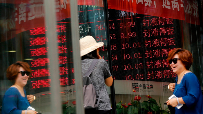 Women chat as they walk by a brokerage house displaying a stock trading index in Beijing
