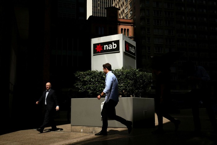 A man walks past a concrete post with the National Australia Bank logo