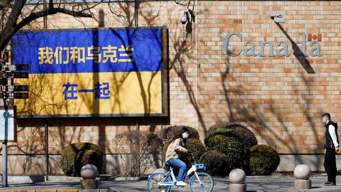 A woman cycles past a billboard supporting Ukraine in the wake of the Russian invasion, outside the Canadian embassy in Beijing