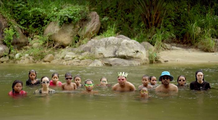 Fifteen people, mostly submerged in a river up to their heads, look at the camera intently