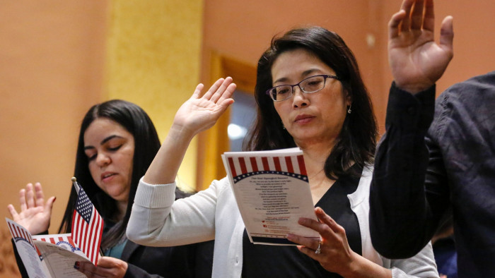 Two women raise their right hands while holding a pamphlet with the naturalisation oath at a citizenship ceremony in New Jersey