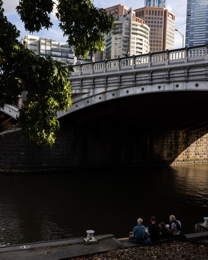 Princes Bridge as viewed from below, with people sitting on the banks of the Yarra