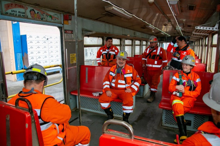 Seven people in mining safety gear are sitting on the train