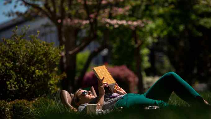 A person lying on their back in the sunshine reading a book