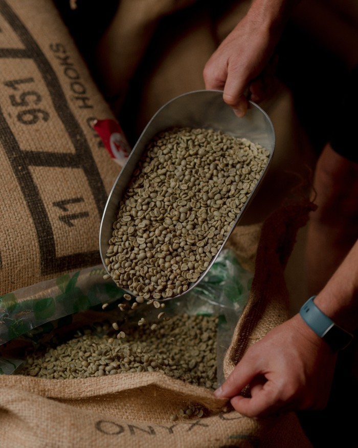 Elysian founder Alistair Durie’s hands scooping coffee beans from a sack with a metallic dish