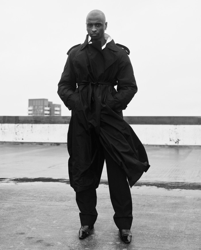 Freelance creative assistant Khari Madu, 27, wears Saint Laurent taffeta coat, £3,615, wool trousers, £1,385, and nappa leather boots, £1,115. Vintage Katharine Hamnett cotton rugby polo shirt (just seen), from stylist’s archive. Earrings, Khari’s own