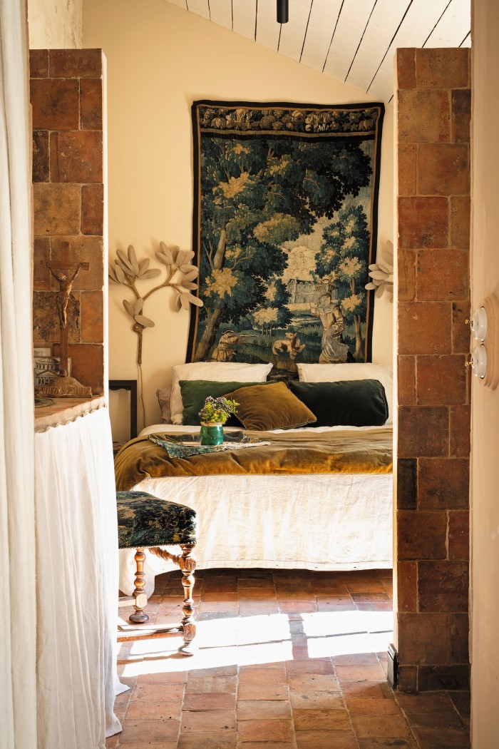 Antique verdure tapestry and traditional Breton floor tiles in a bedroom, with wall sconces by José Esteves