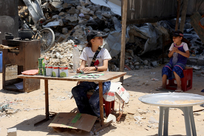 A Palestinian girl sells tins of food in front of destroyed buildings in the Jabalia refugee camp in northern Gaza 
