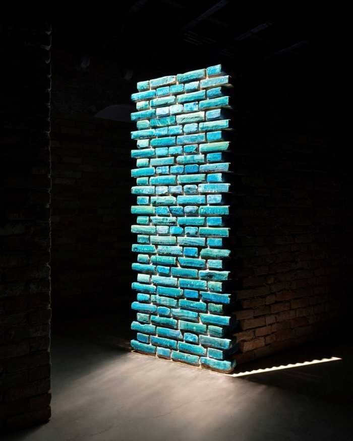 A wall of teal-coloured glazed bricks, brightly lit