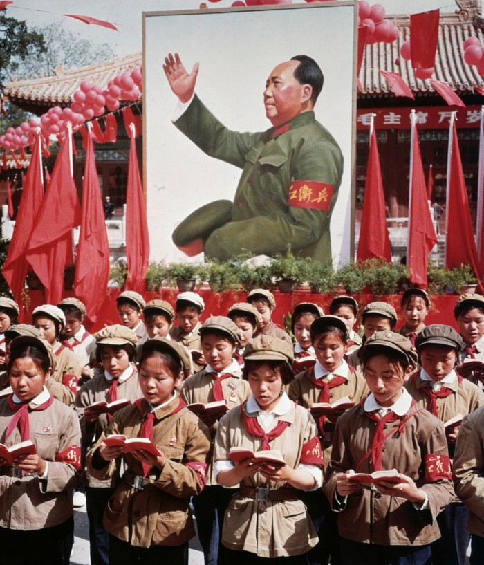 A group of Chinese children in uniform in front of a picture of Chairman Mao Zedong holding Mao’s ‘Little Red Book’ during China’s cultural revolution in 1968