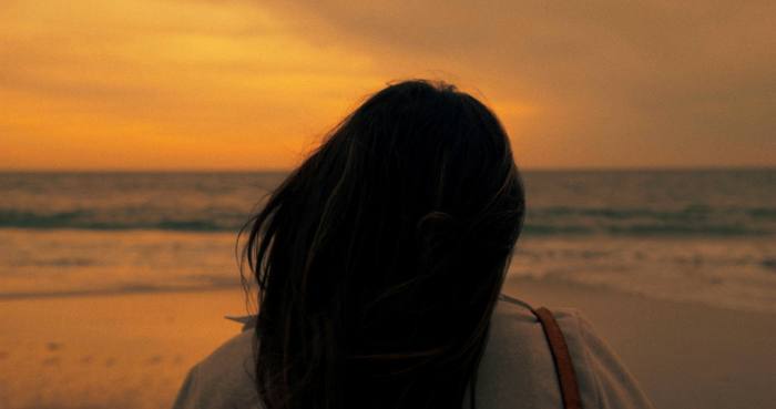 A woman’s head from behind in front of the ocean at sunset