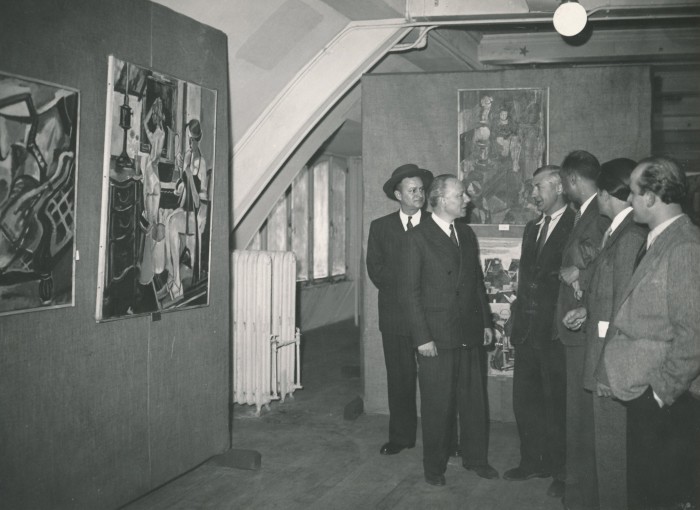 Black and white photo of men in suits looking at paintings